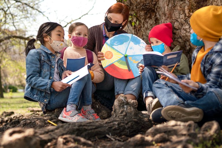 A teacher with small children sitting outdoors in city park, learning group education and social support